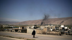 <p>A man walks along a road as smoke rises following attacks early morning, in Basirma, Iraq, on Thursday. Picture: AP Photo/Leo Correa</p>