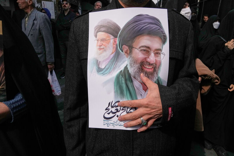 A mourner holds a poster depicting Ayatollah Mojtaba Khamenei, right, the successor to his late father Ayatollah Ali Khamenei, left, as supreme leader. Picture: AP Photo/Vahid Salemi