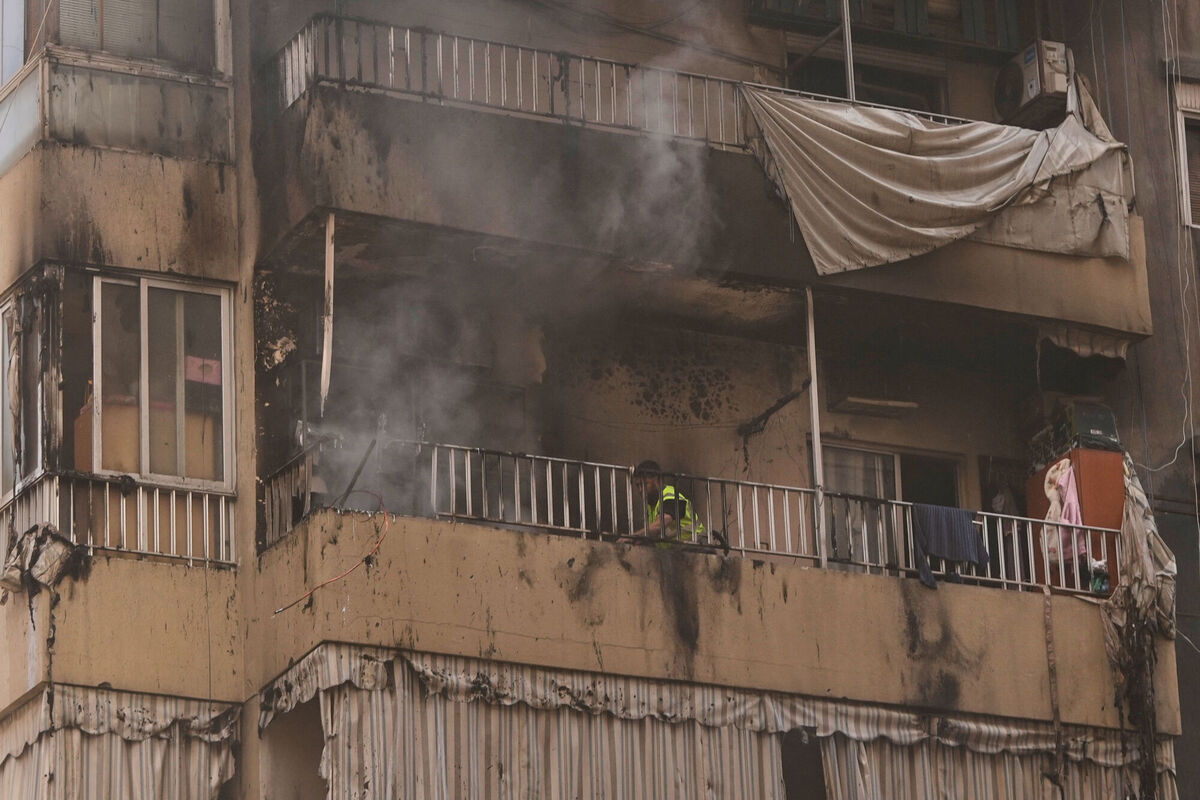 A rescue worker stands on the balcony of a damaged apartment as smoke rises following an Israeli airstrike in central Beirut, Lebanon, Wednesday, March 18, 2026. (AP Photo/Hassan Ammar)