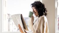 Young woman drinking cup of coffee reading newspaper