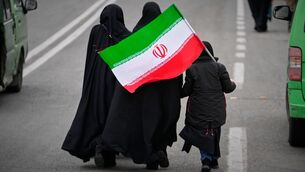 <p>Two women and a child holding an Iranian flag walk toward the Imam Khomeini Grand Mosque to attend Friday prayers in Tehran. Photo: AP/Vahid Salemi</p>