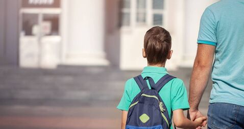 iStock-1126444324.jpg Father leads a little child school boy go hand in hand. Parent and son with backpack behind the back.