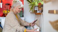 2WTRGAH Senior woman holding mobile phone while adjusting the thermostat on the radiator at home