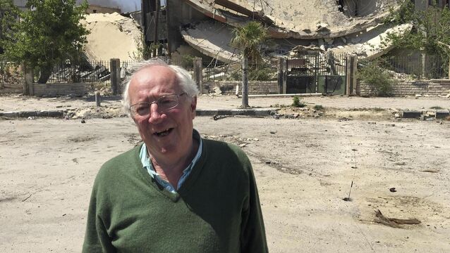 <p>Robert Fisk stands in front of a damaged building in the Damascus suburb of Douma, during a tour by Syria's Information Ministry to the town days after it was captured from rebels by Syrian government forces in 2018. File picture: Bassem Mroue/AP</p>