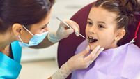 Woman dentist examining smiling child girls teeth with mirror in dental clinic