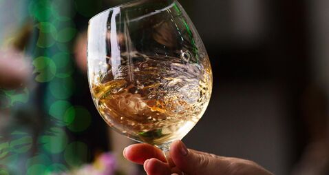 Hand sommelier holding glass of white wine. Swirling wine glass in wine tastings  White wine concept. Wine tour. Vertical, cold