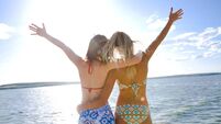 Two bikini-clad girls with outstretched hands near water