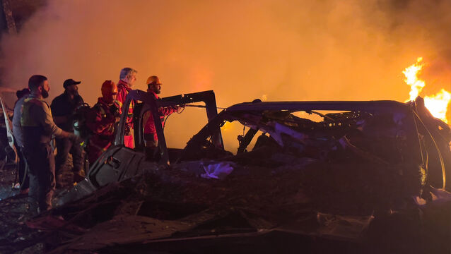 Rescue workers inspect the scene of an Israeli airstrike as fires burn among damaged vehicles, in Beirut, Lebanon (Hussein Malla/AP)