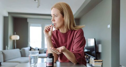 Woman taking supplement at home with water in a wellness lifestyle moment