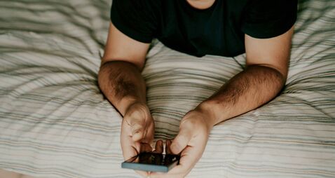 Person using smartphone while relaxing on a comfortable striped bed