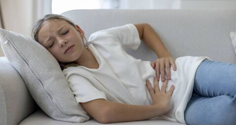 Girl Lying on Sofa with Stomach Ache at Home