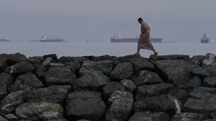 A man walks along the shore as oil tankers and cargo ships line up in the Strait of Hormuz, seen from Khor Fakkan, United Arab Emirates (Altaf Qadri/AP)