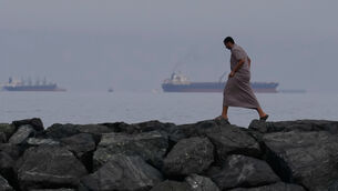 <p>A man walks along the shore as oil tankers and cargo ships line up in the Strait of Hormuz. Picture: AP Photo/Altaf Qadri.</p>
