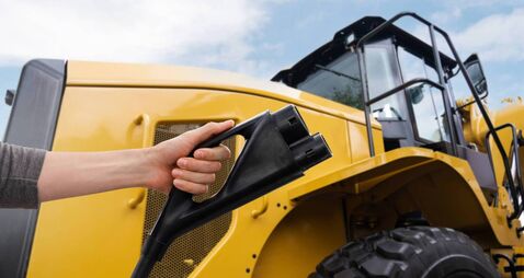 Hand with electric plug on a background of electric tractor