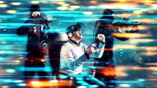 <p>Man wearing a virtual reality headset with two soldiers appear in the background as part of the immersive game the man is playing.</p>