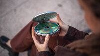 A woman with dreadlocks places a CD into her old CD player to see if it still plays - vintage tech