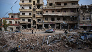 <p>Locals drive past the site of buildings destroyed in an Israeli airstrike (Hassan Ammar/AP)</p>