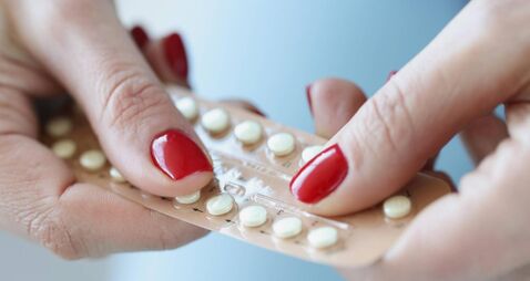 Woman with red manicure holding blister with contraceptive hormonal pills in her hands closeup