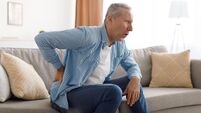 Mature man with side back pain sitting on couch at home