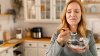 Mature woman eating healthy breakfast with oatmeal, yogurt and blueberries in kichen