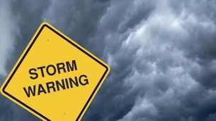A yellow storm warning sign with storm clouds behind