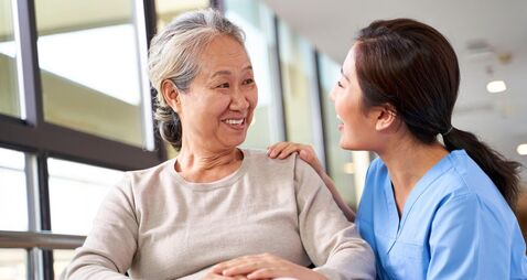 friendly caregiver of nursing home talking to asian senior woman in hallway