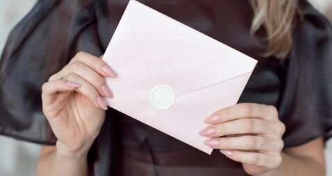 close-up photo of a female hands holding a pink invitation envelope with a wax seal, a gift certificate, a card, a wedding invit