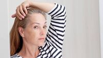 40s woman looking at gray hair in mirror reflection on growth root