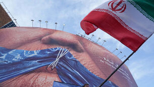 A man waves an Iranian flag for a pro-government campaign under a billboard with graphic showing Strait of Hormuz and sewn lips of US President Donald Trump in a square in central Tehran, Iran (Vahid Salemi/AP)