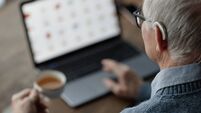Elderly Man Wearing Hearing Aid Working on Laptop at Home while Using Assistive Technology