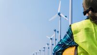 Woman engineer in uniform and holding yellow safety helmet with standing and checking wind turbine power