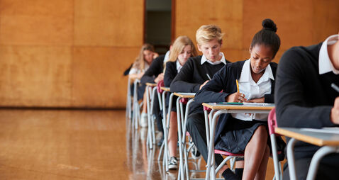 Teenage Students In Uniform Sitting Examination In School Hall