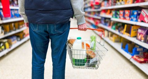 Man holding shopping basket with bread and milk groceries in supermarket