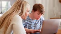 Downs Syndrome Man Sitting With Home Tutor Using Laptop For Lesson At Home