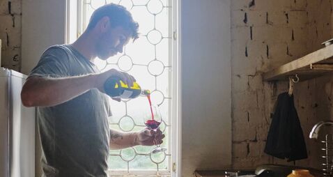 Pouring, kitchen and man with wine, home and alcohol to relax on weekend, window and guy in apartment. Lens flare, break and per