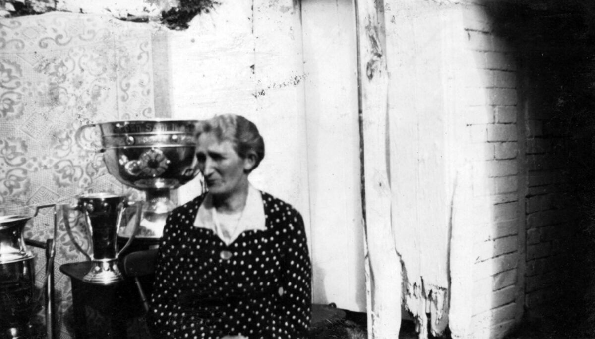 Liam’s grandmother posing in the backyard of her home on Green St, Dingle in 1942, with the Sam Maguire cup, the Munster Championship cup, and the Kerry Football Championship cup, which her son Bill helped to win in 1941 with the Kerry and Dingle teams.
