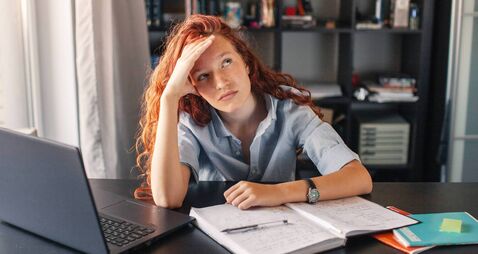 Sad and tired student girl looking on laptop and notebook