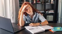 Sad and tired student girl looking on laptop and notebook