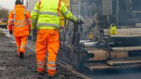 Two construction workers carrying our roadworks laying new asphalt