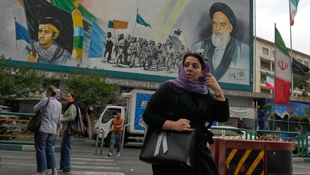 A woman crosses a street in front of a painting of the late Iranian revolutionary founder Ayatollah Khomeini and paramilitary Basij forces in downtown Tehran, Iran (Vahid Salemi/AP)