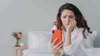 Stressed caucasian woman is doom scrolling. Girl reading morning news on smartphone in her bedroom.