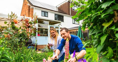 Contented mid adult couple gardening with sustainable solar panel house in background