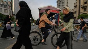 A woman rides a bicycle as others cross a street in central Tehran, Iran (Vahid Salemi/AP)