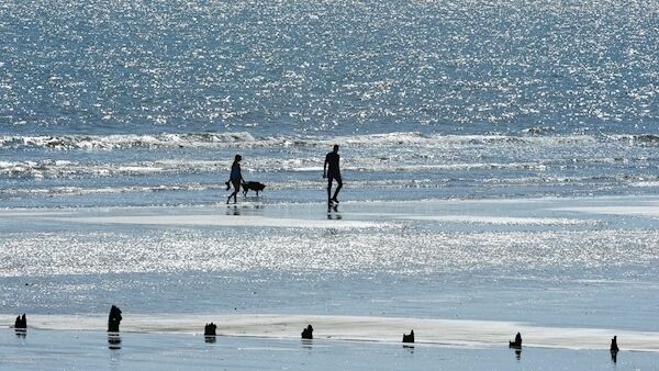 REDBARN beach at Youghal, Co. Cork. Walkers silhouetted against the water, in bright sunshine.