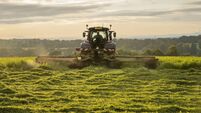 Farm tractor and mower cutting hay field at sunset in Scottish farmland