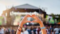 Concertgoer forms heart shape with hands at beachside music festival, crowd enjoys live performance in sunset, love symbol gestu
