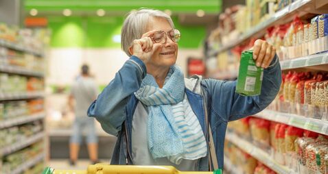 Portrait smiling senior woman making purchases in the supermarket selecting checking a product. Caucasian elderly customer in gr