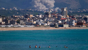 <p>People swim on a public beach as smoke, background, rises from an Israeli airstrike that hit the Qlaileh village, seen from the southern port city of Tyre, Lebanon (Mohammed Zaatari/AP)</p>