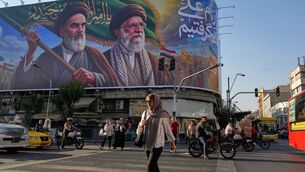 People walk under a banner showing portraits of the late revolutionary founder Ayatollah Khomeini, left, and the slain Supreme Leader Ayatollah Ali Khamenei in Tehran (Vahid Salemi/AP)