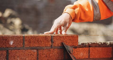 Bricklayer laying another brick in the wall on construction site for sturdy wall